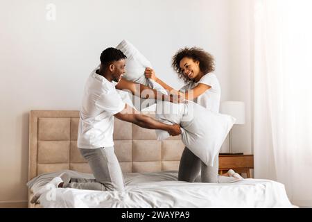 Black Couple Having Pillow Fight Laughing And Flirting In Bedroom Stock Photo