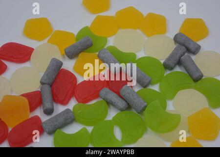 Mix, assorted of unusual branded factory gummy candies in the form of gray, metal cylinders, colored elements, capsules, talismans located on a white. Stock Photo
