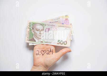 Text 2024 instead of zero, a heart is drawn and on the woman s hand there is 500 hryvnia lying on a white background, help and support in the new year Stock Photo