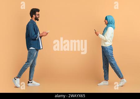 Muslim couple engrossed in their mobile phones while walking past each other Stock Photo