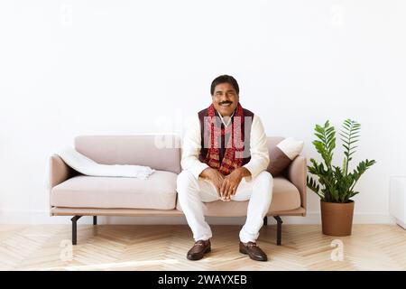 Positive mature indian man sitting on couch in living room Stock Photo