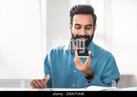 Hindu businessman with beard using voice assistant on phone Stock Photo