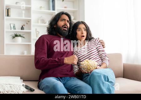 Shocked millennial indian couple watching horror movie on TV Stock Photo