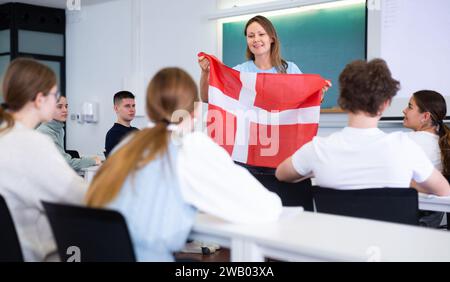 High school teacher tells students about Denmark and holds a Denmark flag in hands. Stock Photo
