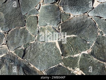 Dark gray and black rustic mosaic nature stonewall from different size and shape parts. Vintage decorative elements. Stock Photo