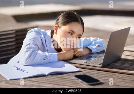 Tired unhappy Korean business lady looking at computer sitting outdoors Stock Photo