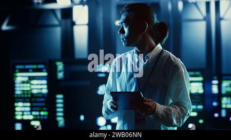 Asian employee walking through data center equipment clusters providing processing resources for different workloads. Productive engineer examining server rigs tasked with solving complex operations Stock Photo