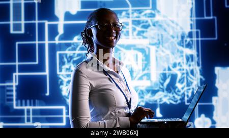 Portrait of happy engineer updating AI systems, writing intricate binary code scripts on laptop. Computer scientist using programming to upgrade artificial intelligence simulation model Stock Photo