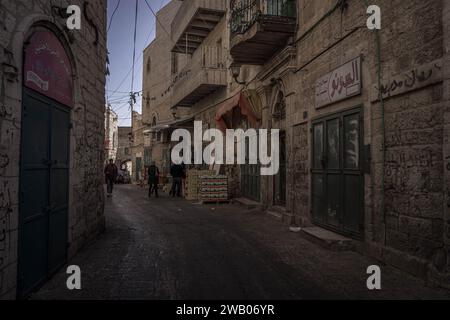 The narrow alley at the old part of Bethlehem city in Palestinian West Bank (Palestine) with Palestinian people passing by the closed shops. Stock Photo