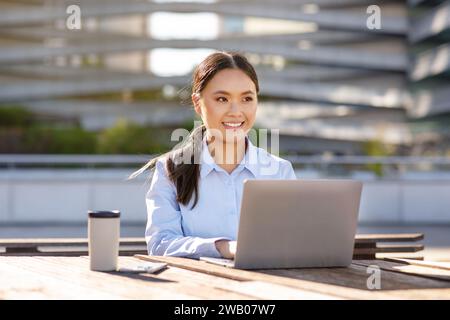 Asian young businesswoman typing on laptop sitting outdoors Stock Photo