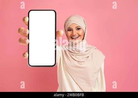 Cheerful arab muslim woman in hijab displaying smartphone with blank white screen Stock Photo