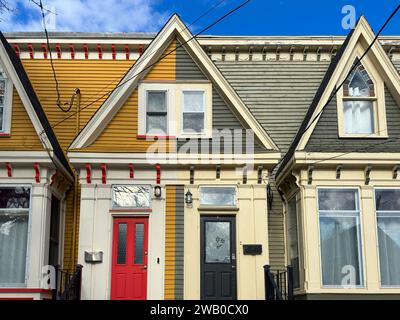 The front entrance to two colorful wooden duplexes. One has a red door the other a black door. Both have letterboxes. There are duplicate windows. Stock Photo