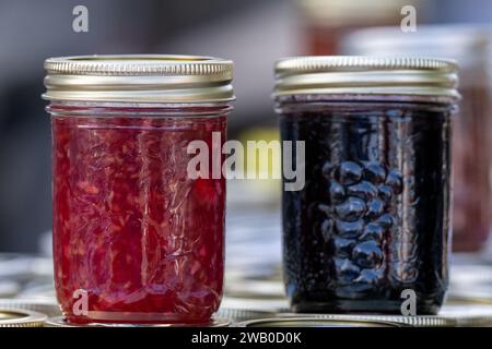 Two small glass jars of various homemade strawberry, raspberry, and blueberry jam for sale at a market. The crocks have metal lids. Stock Photo