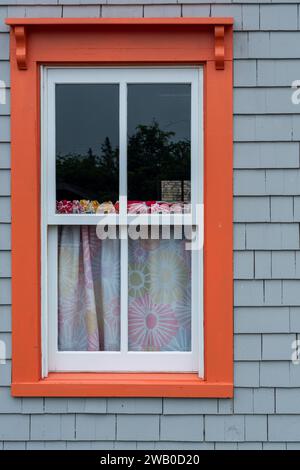 The exterior of a grey wooden house or cottage wall is made of cedar shakes. There's a single vintage glass window with orange decorative wooden trim. Stock Photo