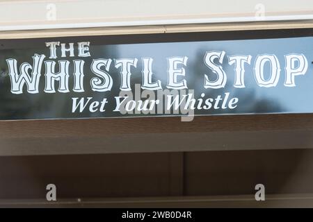 The exterior of a club with a sign over the door. The black banner has white lettering with The Whistle Stop wet your whistle in capital text. Stock Photo