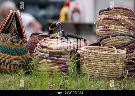 Multiple stacks of different straw hand-weaved baskets with colorful rims. The homemade containers are for sale at a farmers' market. Stock Photo