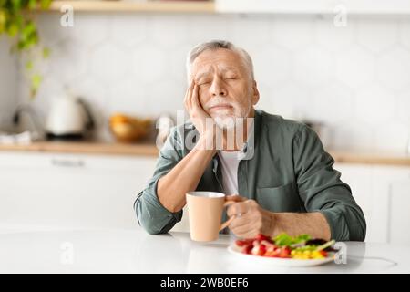 Tired elderly man resting his head on hand, falling asleep during breakfast Stock Photo