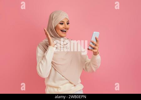 Surprised Young Muslim Woman In Hijab Looking At Smartphone Screen With Excitement Stock Photo
