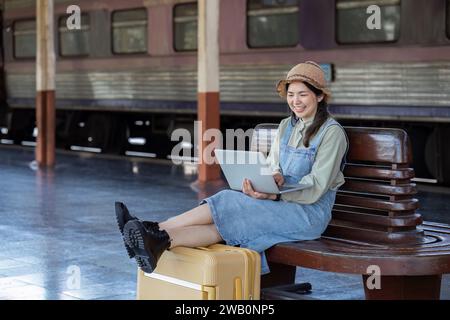 Woman traveler with backpack using laptop to planning vacation on holiday relaxation at the train station Stock Photo
