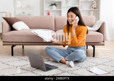 Asian woman freelancer working from home, talking on cell phone Stock Photo