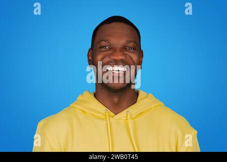 An African man in a yellow hoodie beams with a radiant smile, showcasing white teeth Stock Photo