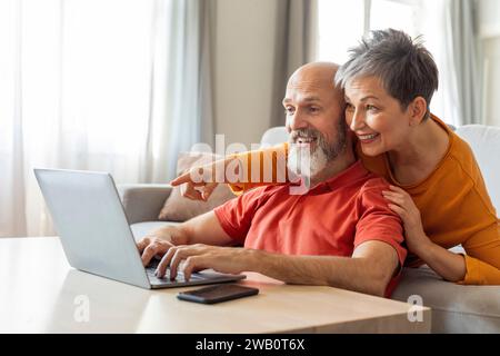 Digital Entertainment. Cheerful Elderly Couple Using Laptop At Home Together Stock Photo