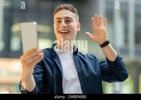 Joyful young man with short curly hair video calling on his smartphone Stock Photo