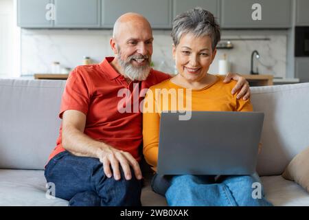 Modern Technologies. Smiling Senior Couple Using Laptop Together At Home Stock Photo