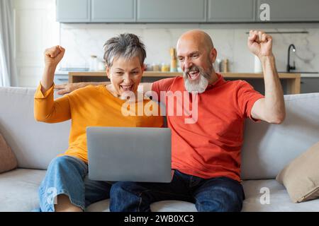 Happy Excited Senior Spouses Celebrating Success With Laptop At Home Stock Photo