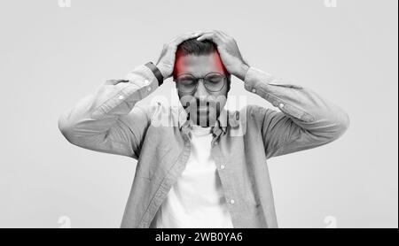 A stressed man in a casual linen shirt and glasses grasps his head in frustration or headache Stock Photo