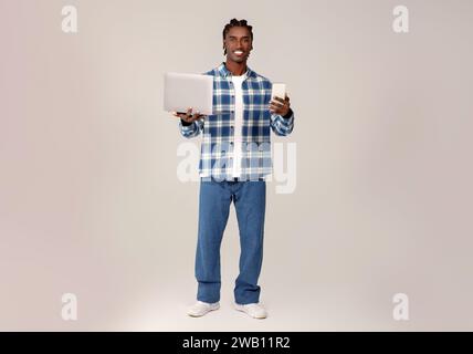 Multitasking young black man holding laptop and smartphone in hands Stock Photo