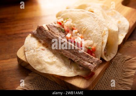 Tacos de Arrachera. Homemade grilled meat in a wheat tortilla. Street food from Mexico, traditionally accompanied with cilantro, onion and spicy sauce Stock Photo