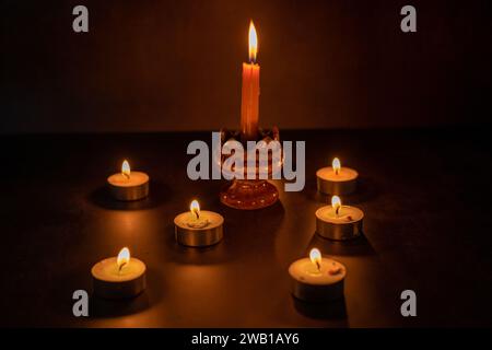 Many candles lit against a black background.Burning candles on dark tableMemory day Stock Photo