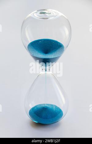Hourglass containing blue sand isolated on white background. Concept of time passing Stock Photo