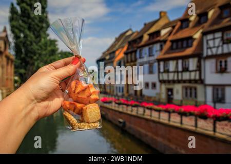 Woman s hand holding a bag of artisanal cookies with half timbered houses above channels of the River Lauch in Petite Venise, Colmar, Alsace, France Stock Photo