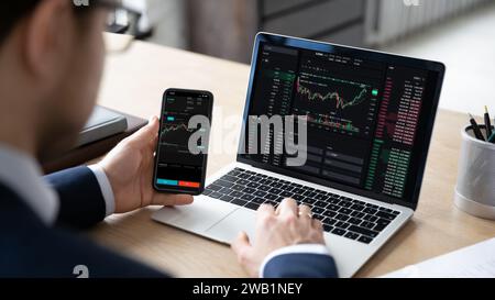 Trader using laptop and smartphone with stock market data Stock Photo