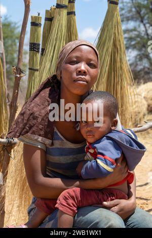 street vendor with the child in the village , young african woman standing in front of a brooms rack in a sunny day on the side of the highway Stock Photo