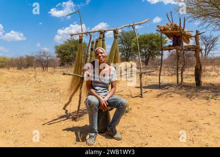 street vendor in the village , young african woman standing in front of a brooms rack in a sunny day on the side of the highway Stock Photo