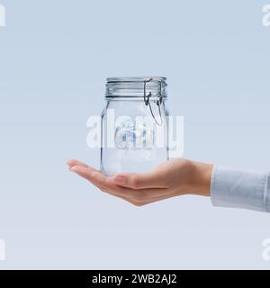 Female hand holding a sealed glass jar containing planet Earth, environmental conservation concept Stock Photo