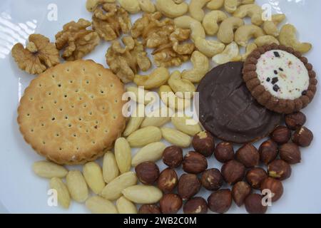 Healthy and wholesome food, snacks, lots of natural nuts: cashews, almonds, walnuts, hazelnuts and biscuits placed on a white glass plate. Stock Photo