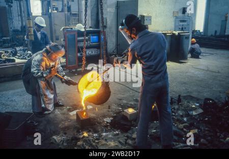 Indonesia, Bandung. Two men pour molten metal into a mold in a steel mill. Stock Photo