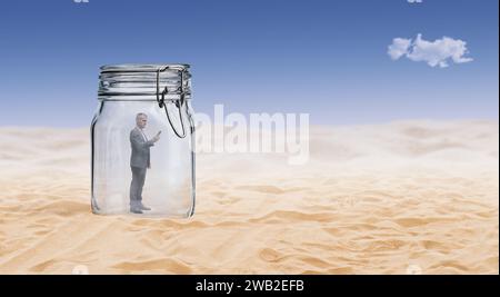 Businessman standing inside a big jar and using a smartphone, he is trapped and lost in the desert Stock Photo