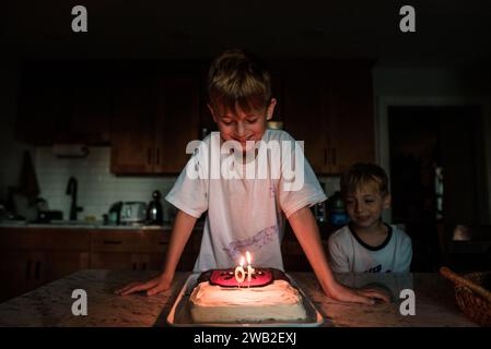 Young boy looks down at lit candles on birthday cake Stock Photo