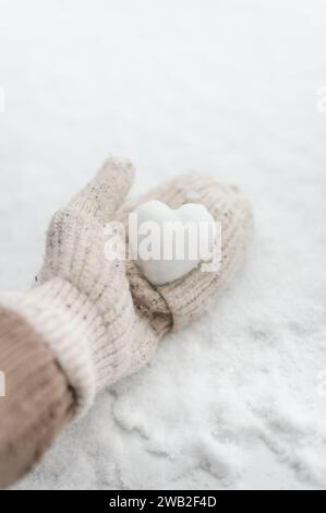Hand in beige mitten holding heart shaped snowball on white background Stock Photo