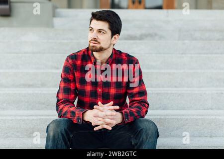 Young man staring off to side sitting on steps outside Stock Photo