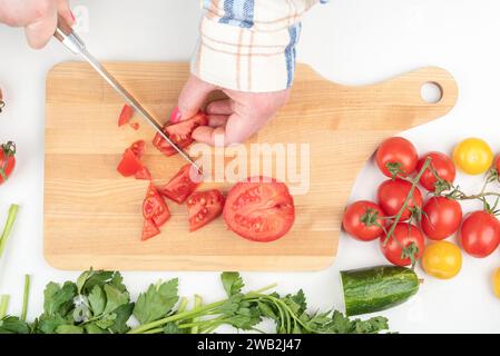 Female hands cut a tomato into small pieces on a cutting board. Home cooking. Stock Photo