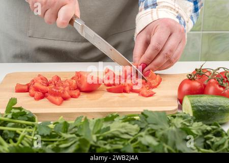 A juicy tomato is cut into small pieces on a wooden cutting board. Home cooking. Stock Photo
