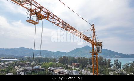 Close-up view from a drone of a construction crane cabin against the backdrop of beautiful sea, sky and mountain. Construction concept Stock Photo