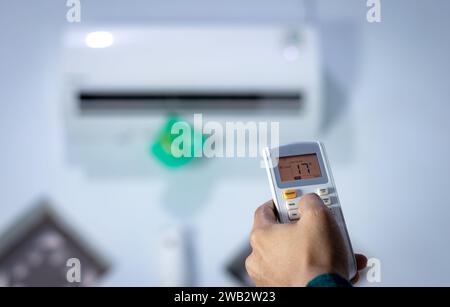 Man's hand with remote control directed at air conditioner. Stock Photo