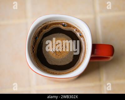 Red cup (white inside) of freshly brewed coffee on a ceramic tile countertop Stock Photo
